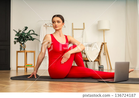 Woman does yoga at home using a laptop for guidance 136724187