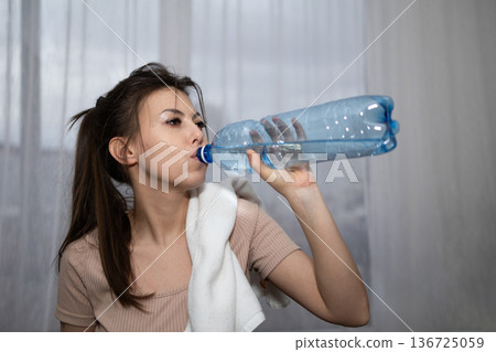 Woman Drinks Water While Holding a Towel in a Room With Natural Light During Daytime Woman Drinks Water While Holding a Towel in a Room With Natural Light During Daytime 136725059