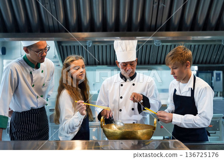 Chef teacher teaches cooking to the group children in class kitchen room. Chef teacher teaches cooking to the group children in class kitchen room. 136725176