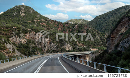 Winding mountain road with asphalt curves leading to a majestic rocky peak under a blue cloudy sky. Beautiful scenic landscape for travel and adventure concepts Winding mountain road with asphalt curves leading to a majestic rocky peak under a blue cloudy sky. Beautiful scenic landscape for travel and adventure concepts 136725788