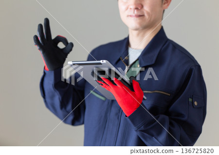 A middle-aged male businessman in work clothes holding a tablet and making a circle sign 136725820