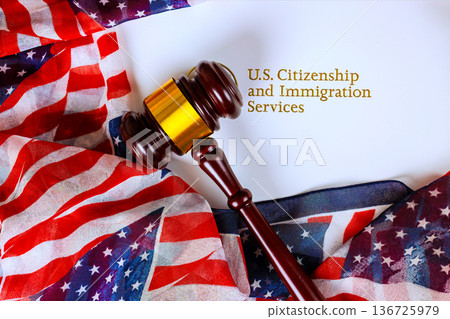 Law gavel is placed on folded American flags U.S. Citizenship Immigration Services in prominent layout. 136725979