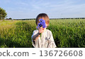 A beautiful happy little baby stands on a green meadow. Cute baby in a field of flowers. A handsome child holds a bouquet of wildflowers and gestures that he is giving them to his mother. 136726608