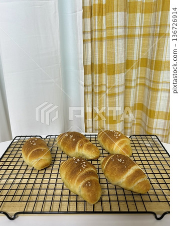 Golden brown salt bread with a soft, fluffy interior and a perfectly crisp crust, lightly sprinkled with coarse salt for a savory touch. A simple yet satisfying treat for any occasion. 136726914