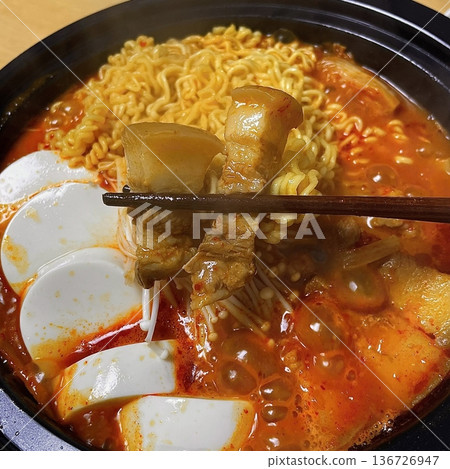 A hearty bowl of Budaejjigae (Korean Army Stew), filled with sausage, tofu, kimchi, and noodles in a spicy broth. This flavorful dish brings warmth and comfort, perfect for sharing. 136726947