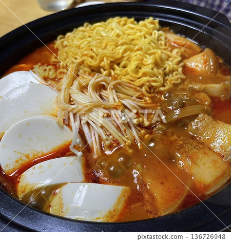 A hearty bowl of Budaejjigae (Korean Army Stew), filled with sausage, tofu, kimchi, and noodles in a spicy broth. This flavorful dish brings warmth and comfort, perfect for sharing. 136726948