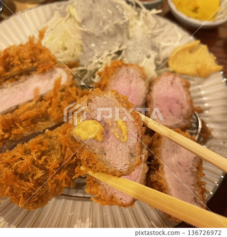 Crispy tonkatsu, a Japanese-style breaded and deep-fried pork cutlet, served with shredded cabbage and drizzled with savory sauce. A delightful balance of crunchy texture and juicy meat. 136726972