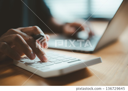 Close-up of Person Using Calculator and Laptop for Financial Calculations Close-up of Person Using Calculator and Laptop for Financial Calculations 136729645