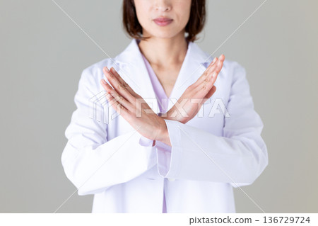 一位身穿白大褂的中年女醫生正在比劃十字。 一位身穿白大褂的中年女醫生正在比劃十字。 136729724