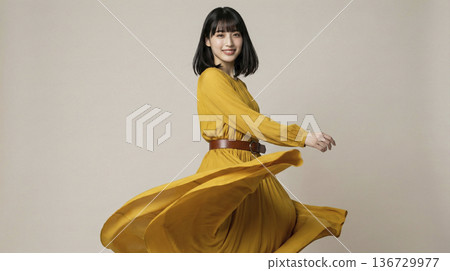 一位微笑的日本女子身穿飄動的黃色長裙，旋轉著身體。 136729977