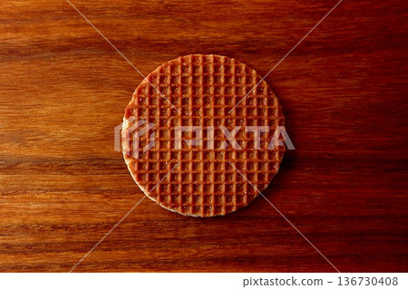 A stroopwafel split in two on a wood grain background, viewed from above 136730408