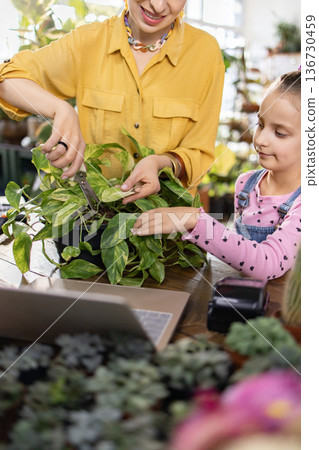 A woman and a young girl are trimming a houseplant together, enjoying a moment of gardening 136730459