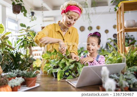 A woman and a young girl are learning about plants and gardening together, using a laptop for information 136730467