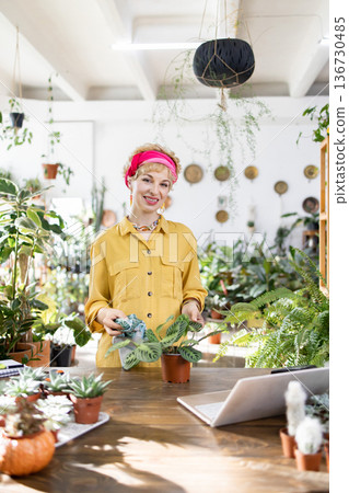 A woman smiles while tending to plants in a bright and airy shop filled with greenery A woman smiles while tending to plants in a bright and airy shop filled with greenery 136730485