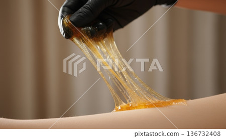 Close up of gloved hand applying sugaring paste for depilation on human skin 136732408