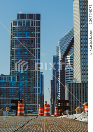 Construction work takes place in a city area filled with tall buildings during a sunny day 136734071