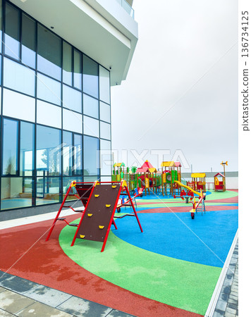 Colorful playground with climbing frame and slides located near a modern building in an urban area during cloudy weather Colorful playground with climbing frame and slides located near a modern building in an urban area during cloudy weather 136734125
