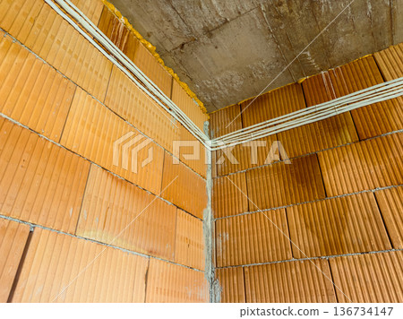 Construction work shows a corner with brick walls and electrical wiring in a building under renovation in a city setting during day hours 136734147