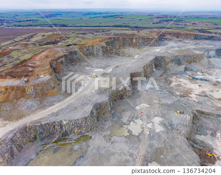 Large quarry site showing excavation work and heavy machinery in a rural area under cloudy skies Large quarry site showing excavation work and heavy machinery in a rural area under cloudy skies 136734204