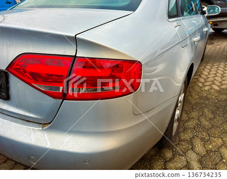 Damaged silver car parked in a lot with multiple vehicles and clear blue sky in the background during the day Damaged silver car parked in a lot with multiple vehicles and clear blue sky in the background during the day 136734235