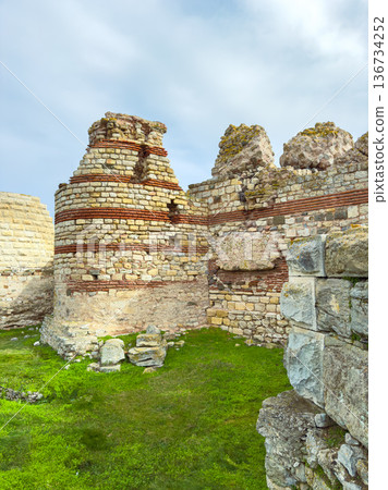 Exploring ancient stone ruins at a historical site during the day with clear skies and green grass surrounding the area Exploring ancient stone ruins at a historical site during the day with clear skies and green grass surrounding the area 136734252