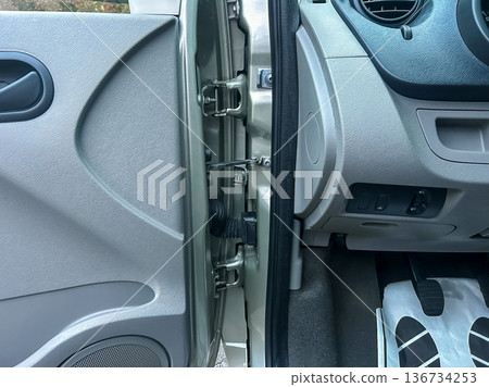 Car door interior shows latch mechanism with detailed view of the door handle, panel, and flooring during daylight, showcasing the workings of a vehicle entry system 136734253