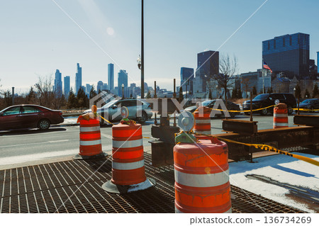 Construction barriers line the road with a city skyline in the background during the daytime in a busy urban area 136734269