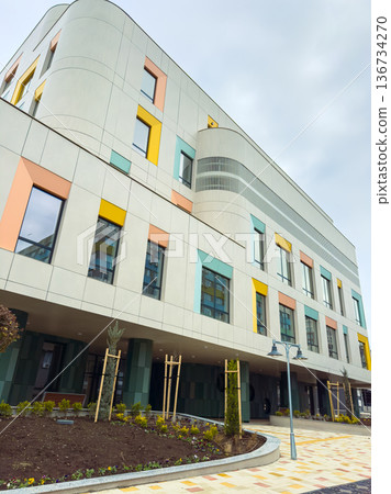 New building in urban area shows colorful facade and landscaping next to sidewalk in daytime during overcast weather 136734270