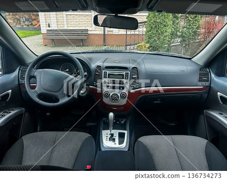 Car interior view showing dashboard, steering wheel, and gear shift with various controls during daytime in a private location 136734273