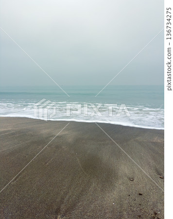 Beach waves meet wet sand under a gray sky near the ocean at dawn with soft sounds of water and distant horizons Beach waves meet wet sand under a gray sky near the ocean at dawn with soft sounds of water and distant horizons 136734275