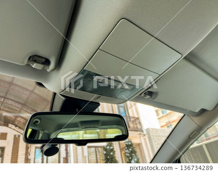 Car interior view showing the overhead console and rearview mirror in a parked vehicle in a residential area during daytime Car interior view showing the overhead console and rearview mirror in a parked vehicle in a residential area during daytime 136734289