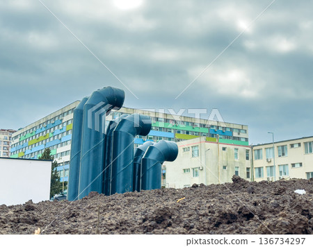 Construction site features pipes rising from soil near buildings under an overcast sky in an urban area during the day Construction site features pipes rising from soil near buildings under an overcast sky in an urban area during the day 136734297