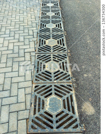 Metal grates are placed on a paved pathway in a city, showing their pattern and design during daytime Metal grates are placed on a paved pathway in a city, showing their pattern and design during daytime 136734300