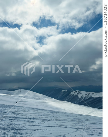 Wide view of a snowy landscape with mountains and clouds during winter in a remote area 136734328