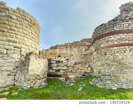Historic stone ruins stand in an open area with grass and clear sky in the background during the daytime around a historical site Historic stone ruins stand in an open area with grass and clear sky in the background during the daytime around a historical site 136734329