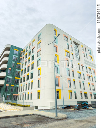 New building stands tall with colorful accents in a modern urban area near a busy road during cloudy weather New building stands tall with colorful accents in a modern urban area near a busy road during cloudy weather 136734345