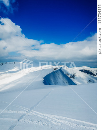 Snow-covered hills under a clear blue sky with some clouds in the background this winter scene shows a serene landscape of nature and cold weather Snow-covered hills under a clear blue sky with some clouds in the background this winter scene shows a serene landscape of nature and cold weather 136734353