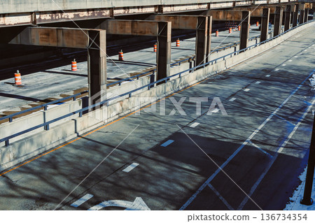 Empty highway beneath a structure with traffic cones in a city during daylight hours Empty highway beneath a structure with traffic cones in a city during daylight hours 136734354