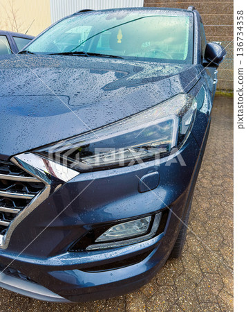 Close view of a dark blue car parked under cloudy skies with water droplets on the surface Close view of a dark blue car parked under cloudy skies with water droplets on the surface 136734358