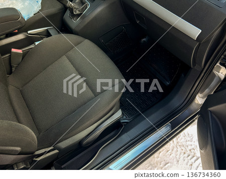 Car interior shows driver's seat and dashboard with floor mat in a parked vehicle during daylight hours Car interior shows driver's seat and dashboard with floor mat in a parked vehicle during daylight hours 136734360