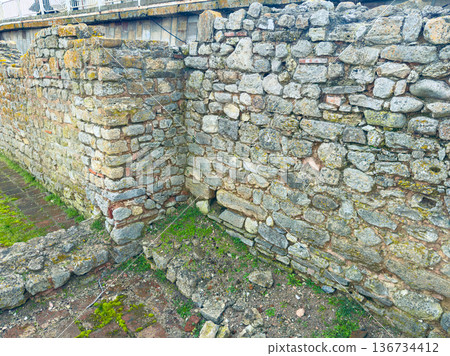 Old stone walls show ancient construction methods at a historic site near a modern area on a clear day Old stone walls show ancient construction methods at a historic site near a modern area on a clear day 136734412