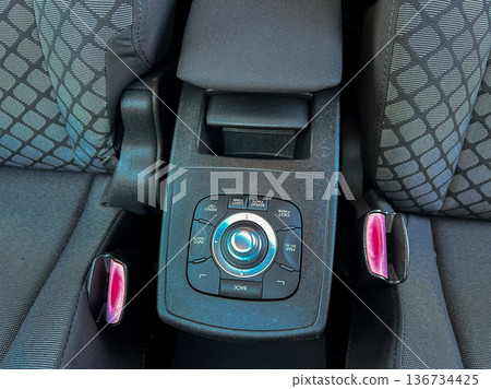 Center console with control buttons in a vehicle with dark fabric seats captured during daylight 136734425