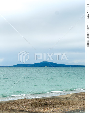 Cloudy skies above the water with distant mountains and shoreline during the day near a beach location 136734443