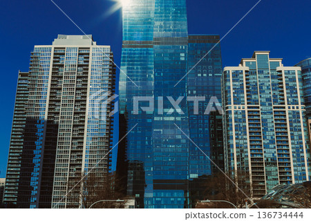 Clean glass buildings stand under a blue sky on a sunny day in a city with many tall structures and busy streets Clean glass buildings stand under a blue sky on a sunny day in a city with many tall structures and busy streets 136734444