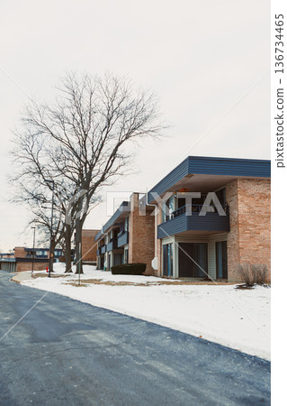 Snow covers buildings in a quiet neighborhood during winter on a cloudy day with bare trees lining the street Snow covers buildings in a quiet neighborhood during winter on a cloudy day with bare trees lining the street 136734465