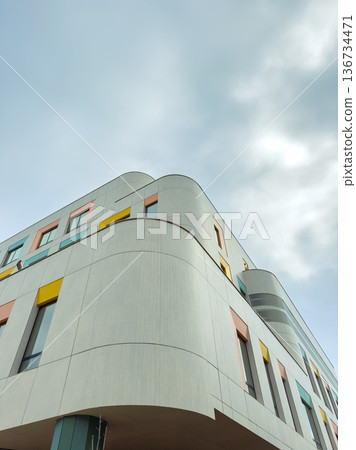 Modern building design in an urban area showcases unique architecture against a cloudy sky in the late afternoon light 136734471