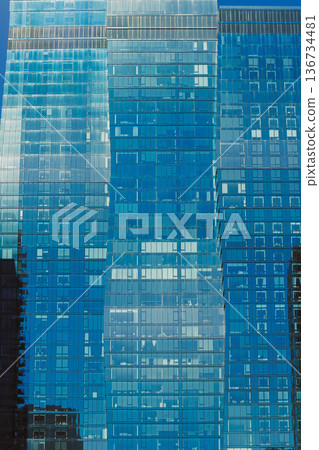 Modern glass buildings reflect the blue sky and surrounding cityscape during midday in an urban setting Modern glass buildings reflect the blue sky and surrounding cityscape during midday in an urban setting 136734481