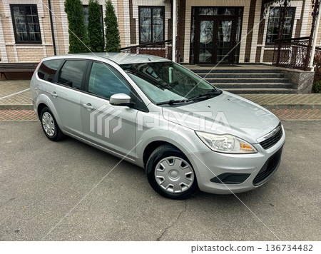 Silver car parked outside a building with steps and green trees in a suburban area during daylight hours Silver car parked outside a building with steps and green trees in a suburban area during daylight hours 136734482