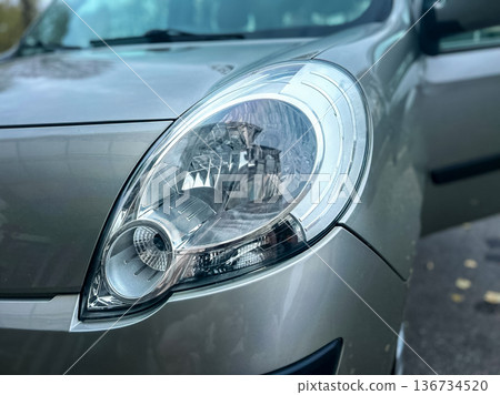 Close up view of a car headlight with open door and shiny surface in an urban area during daylight hours Close up view of a car headlight with open door and shiny surface in an urban area during daylight hours 136734520