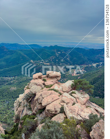View from mountain peak showing rocky formation and green landscape under gray sky with distant hills and valleys View from mountain peak showing rocky formation and green landscape under gray sky with distant hills and valleys 136734528